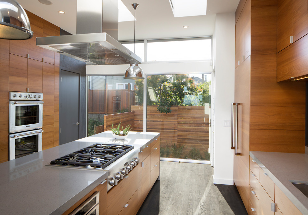 Moderne Küche mit flächenbündigen Schrankfronten, hellbraunen Holzschränken, Quarzwerkstein-Arbeitsplatte, Kücheninsel, grauer Arbeitsplatte, dunklem Holzboden und braunem Boden in San Francisco