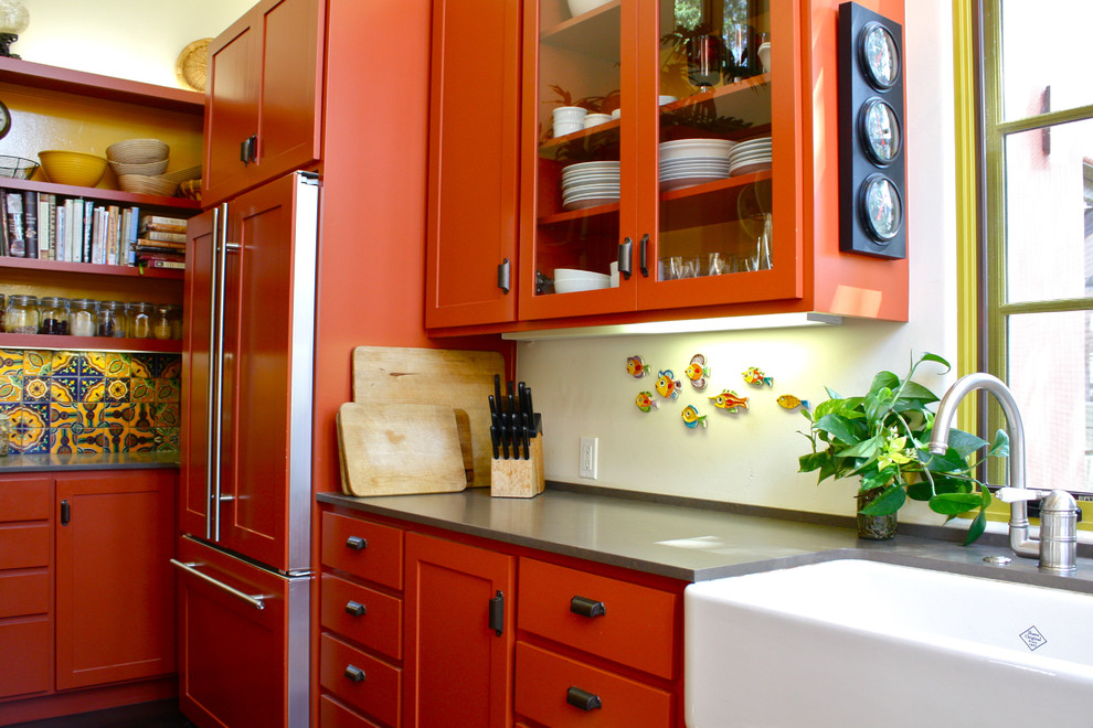 サンタバーバラにあるサンタフェスタイルのおしゃれなキッチン (ガラス扉のキャビネット、エプロンフロントシンク、オレンジのキャビネット、パネルと同色の調理設備) の写真
