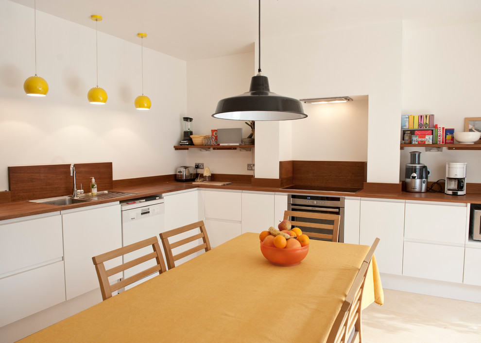 На фото: угловая кухня в современном стиле с обеденным столом, накладной мойкой, плоскими фасадами, белыми фасадами и техникой из нержавеющей стали с