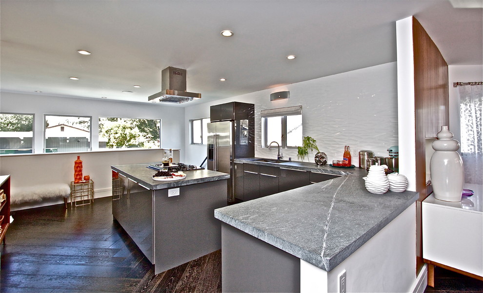 Inredning av ett 60 tals mellanstort kök med öppen planlösning, med släta luckor, grå skåp, marmorbänkskiva, rostfria vitvaror, betonggolv och en köksö