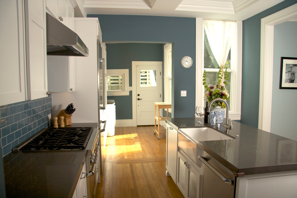 Example of a mid-sized transitional single-wall light wood floor eat-in kitchen design in San Francisco with an integrated sink, shaker cabinets, white cabinets, solid surface countertops, blue backsplash, glass tile backsplash and stainless steel appliances