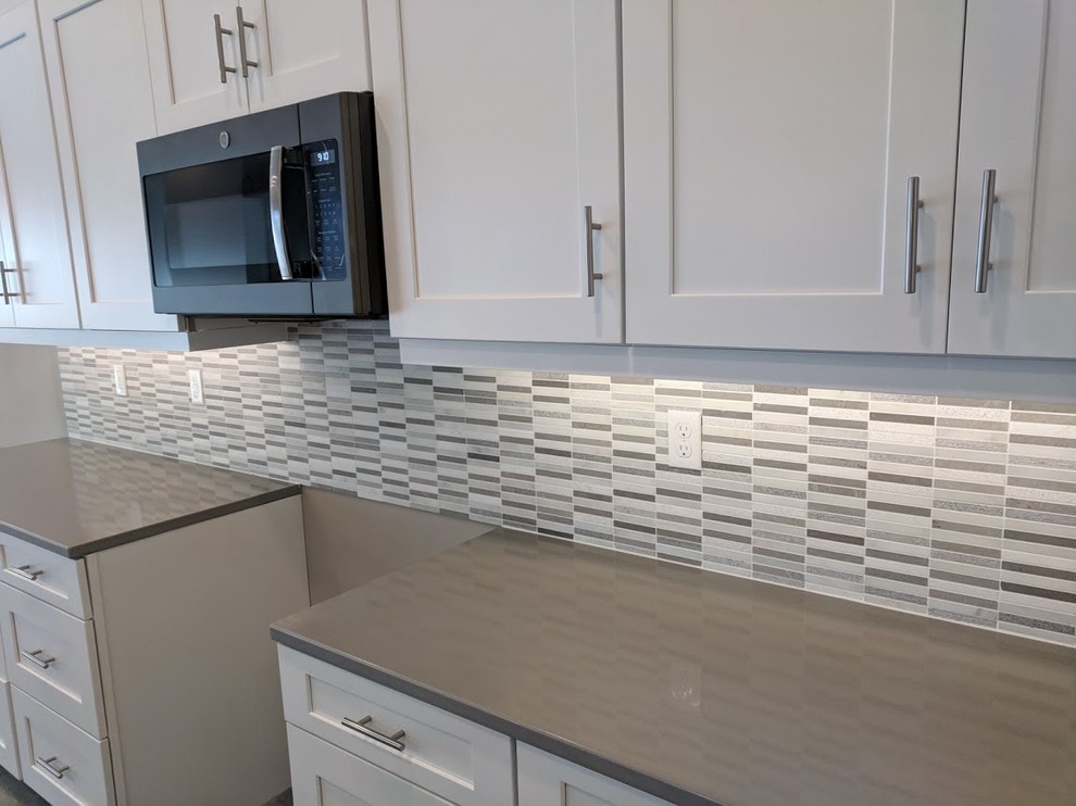 Large contemporary l-shaped open plan kitchen with a submerged sink, recessed-panel cabinets, white cabinets, grey splashback, mosaic tiled splashback, stainless steel appliances, porcelain flooring, an island, grey floors and engineered stone countertops.