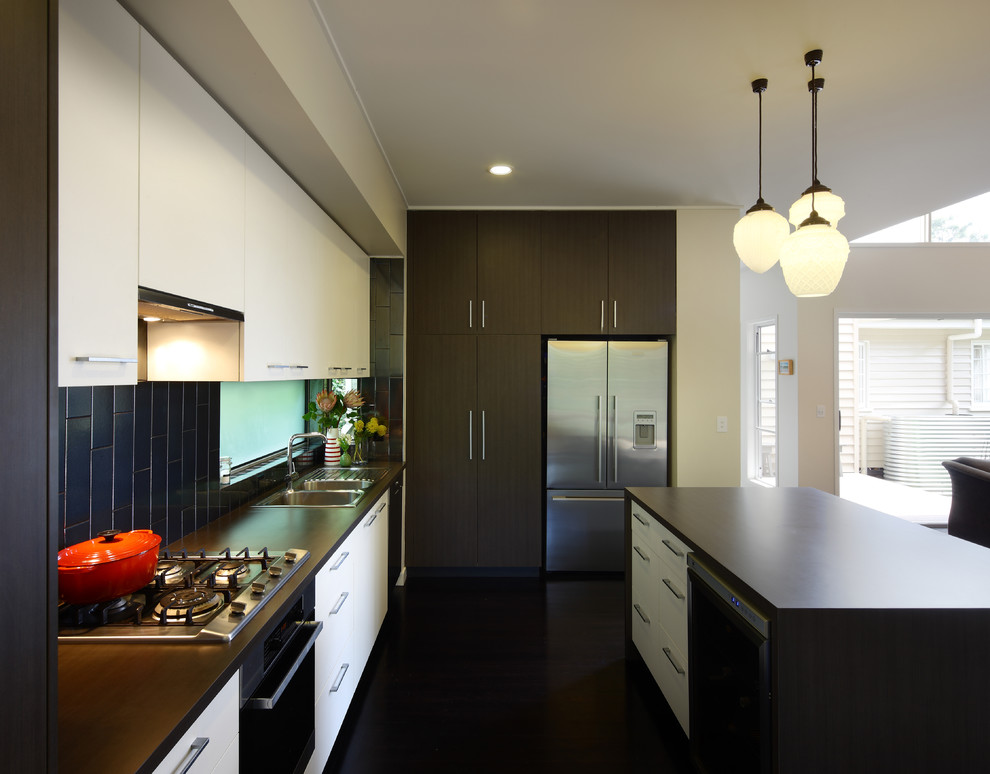 Exempel på ett mellanstort modernt kök, med en nedsänkt diskho, släta luckor, vita skåp, svart stänkskydd, rostfria vitvaror, laminatbänkskiva, stänkskydd i keramik, mörkt trägolv och en köksö