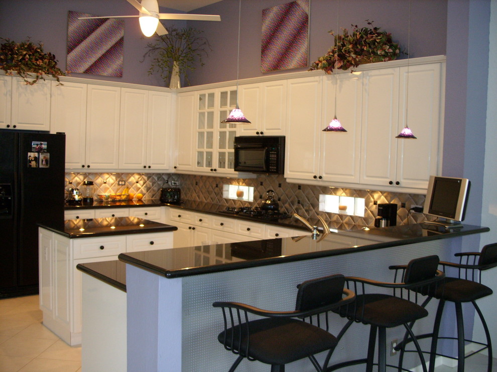 マイアミにある高級な中くらいなコンテンポラリースタイルのおしゃれなキッチン (レイズドパネル扉のキャビネット、白いキャビネット、御影石カウンター、メタリックのキッチンパネル、メタルタイルのキッチンパネル、黒い調理設備、セラミックタイルの床、ベージュの床、黒いキッチンカウンター) の写真