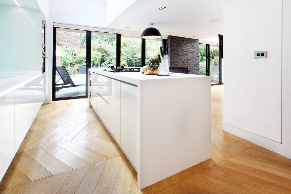 This is an example of a medium sized contemporary l-shaped open plan kitchen in Manchester with a built-in sink, flat-panel cabinets, white cabinets, light hardwood flooring and an island.