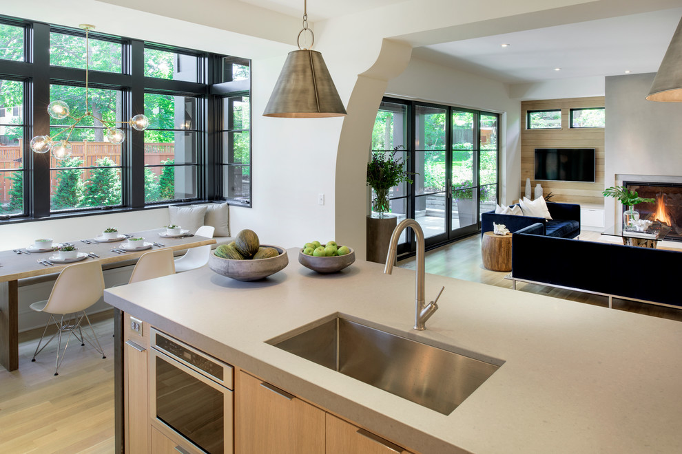 Large transitional l-shaped light wood floor open concept kitchen photo in Minneapolis with an undermount sink, flat-panel cabinets, white cabinets, solid surface countertops, white backsplash, stone slab backsplash, paneled appliances and an island