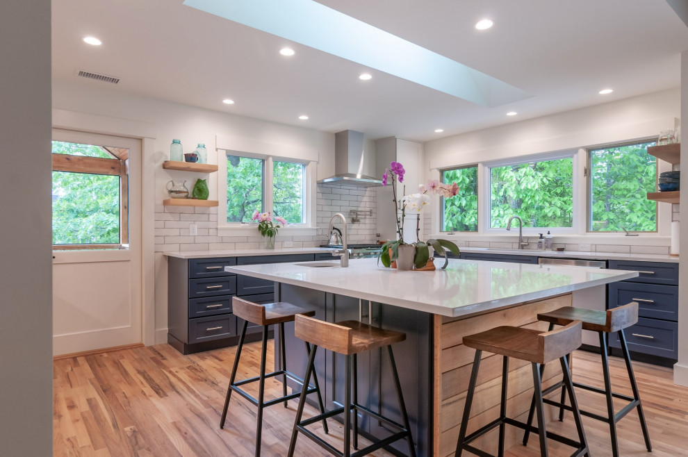 Inspiration for a transitional l-shaped medium tone wood floor and brown floor kitchen remodel in Charlotte with an undermount sink, shaker cabinets, blue cabinets, white backsplash, subway tile backsplash, stainless steel appliances, an island and white countertops