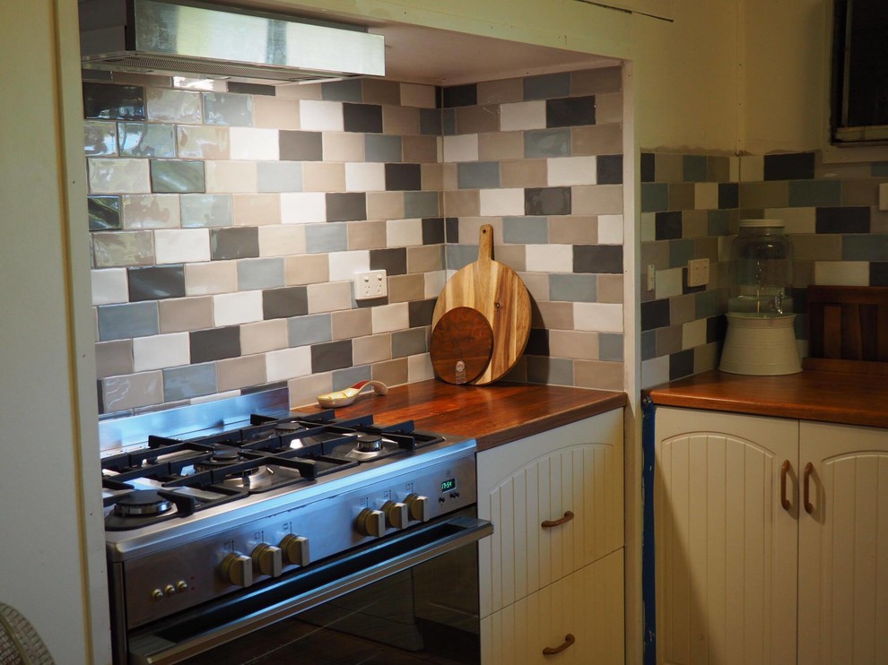На фото: кухня в стиле кантри с деревянной столешницей и разноцветным фартуком с