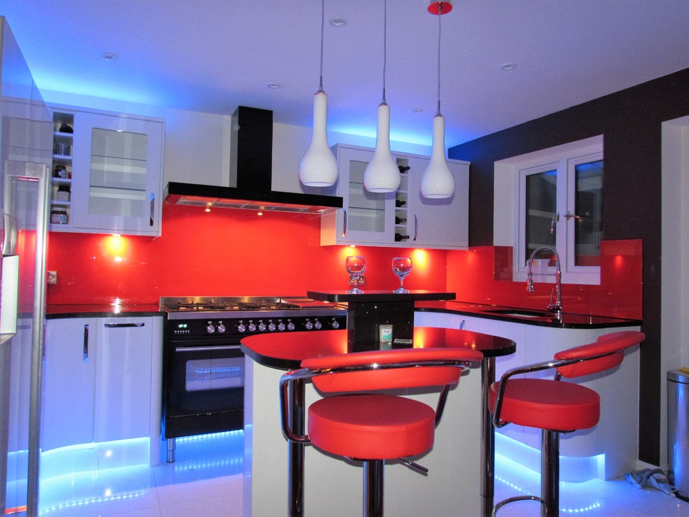 Inredning av ett modernt stort kök, med en enkel diskho, vita skåp, granitbänkskiva, rött stänkskydd, glaspanel som stänkskydd, svarta vitvaror, marmorgolv och en halv köksö
