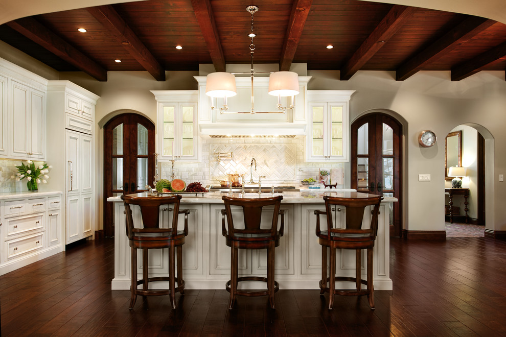 Open concept kitchen - mid-sized traditional l-shaped dark wood floor and brown floor open concept kitchen idea in Phoenix with a farmhouse sink, recessed-panel cabinets, white cabinets, marble countertops, white backsplash, stone tile backsplash, stainless steel appliances and an island