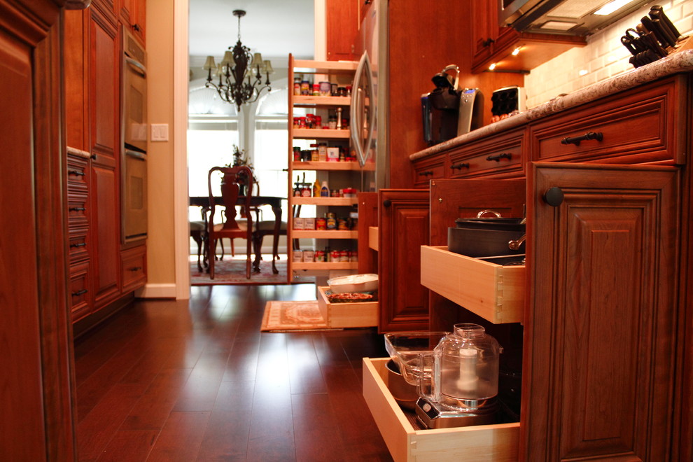 Exempel på ett mellanstort klassiskt kök, med en undermonterad diskho, luckor med upphöjd panel, skåp i mellenmörkt trä, bänkskiva i täljsten, grått stänkskydd, stänkskydd i stenkakel, rostfria vitvaror, mellanmörkt trägolv och en halv köksö