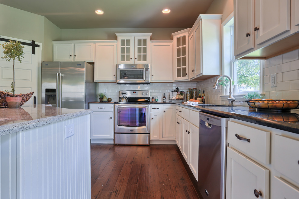 Example of a mid-sized classic u-shaped medium tone wood floor open concept kitchen design in Other with recessed-panel cabinets, white cabinets, granite countertops, white backsplash, stainless steel appliances, an island and an undermount sink