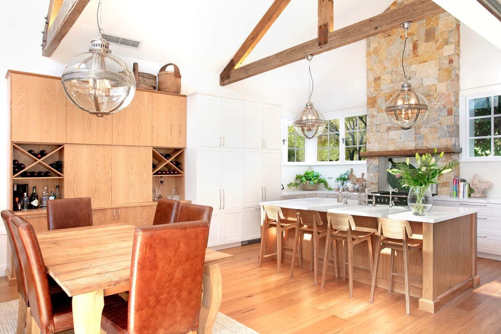 Example of a large cottage l-shaped light wood floor and beige floor eat-in kitchen design in Sydney with a farmhouse sink, shaker cabinets, beige cabinets, solid surface countertops, beige backsplash, paneled appliances and an island