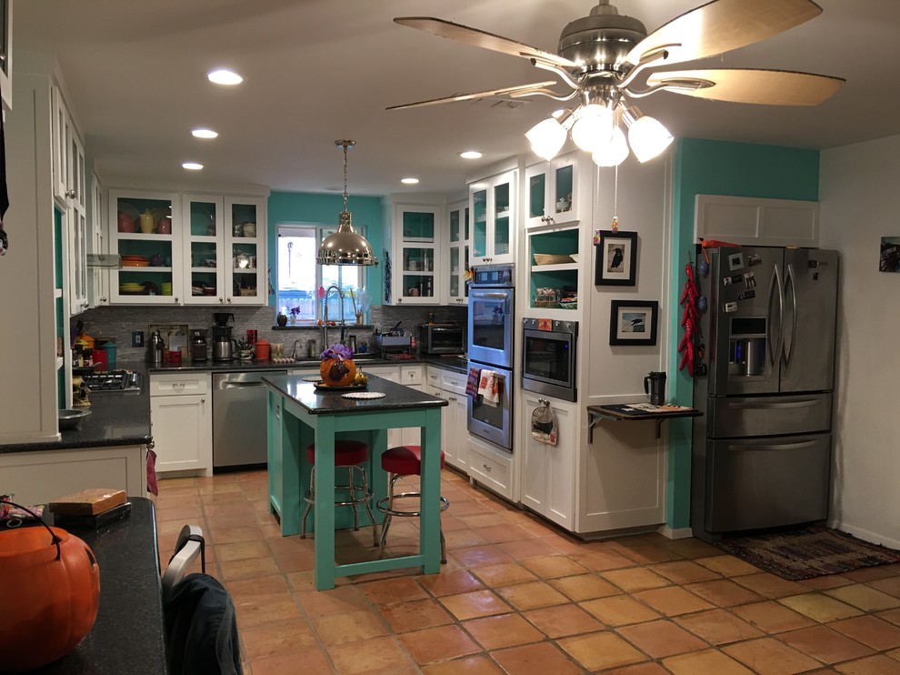 Foto på ett mellanstort eklektiskt kök, med en undermonterad diskho, luckor med glaspanel, vita skåp, granitbänkskiva, grått stänkskydd, stänkskydd i glaskakel, rostfria vitvaror, klinkergolv i terrakotta, en köksö och beiget golv