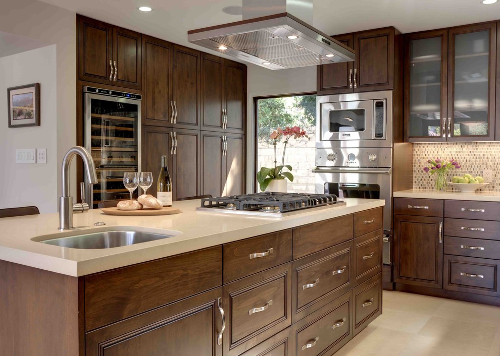 This is an example of a large contemporary l-shaped kitchen/diner in Los Angeles with raised-panel cabinets, mosaic tiled splashback, stainless steel appliances, dark wood cabinets, a submerged sink, an island, engineered stone countertops, multi-coloured splashback and limestone flooring.