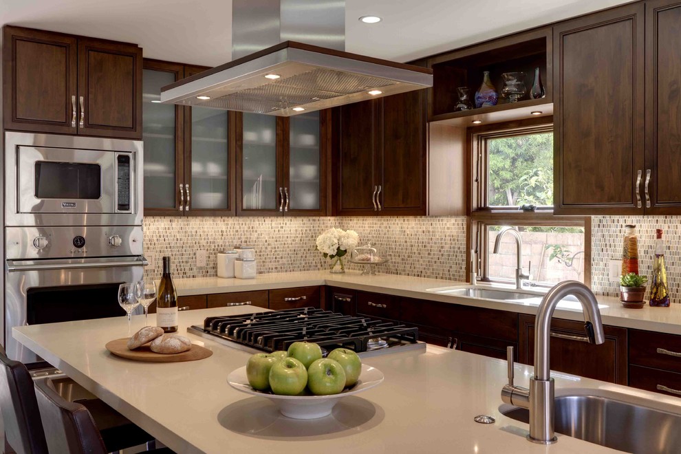 Mid-sized trendy l-shaped limestone floor eat-in kitchen photo in Los Angeles with an undermount sink, raised-panel cabinets, dark wood cabinets, multicolored backsplash, glass tile backsplash, stainless steel appliances, an island and quartz countertops