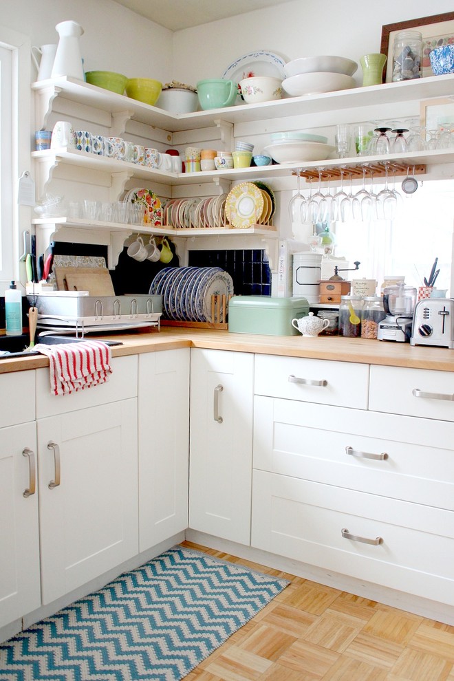 Diseño de cocina romántica cerrada con armarios con paneles empotrados, puertas de armario blancas, encimera de madera, salpicadero negro, suelo de madera clara y fregadero encastrado