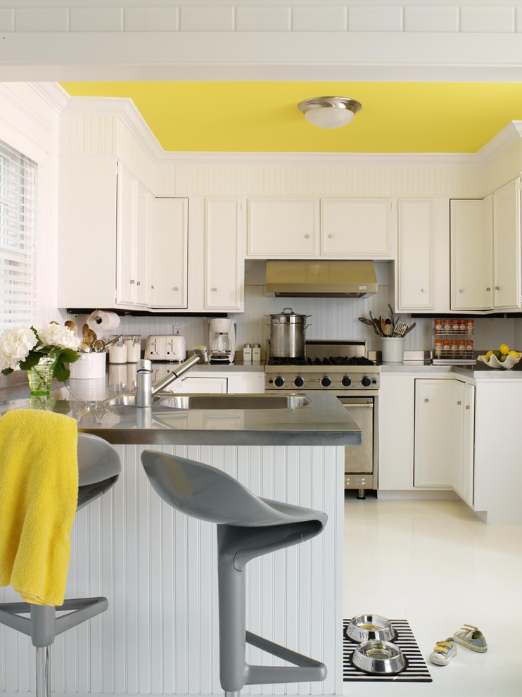 Inspiration for a mid-sized contemporary u-shaped laminate floor and white floor eat-in kitchen remodel in New York with recessed-panel cabinets, white cabinets, stainless steel appliances, a double-bowl sink, solid surface countertops, white backsplash, a peninsula and gray countertops