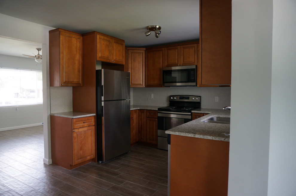 Foto på ett litet retro grön kök, med en dubbel diskho, luckor med upphöjd panel, skåp i mellenmörkt trä, granitbänkskiva, vitt stänkskydd, stänkskydd i mosaik, rostfria vitvaror, klinkergolv i porslin och brunt golv