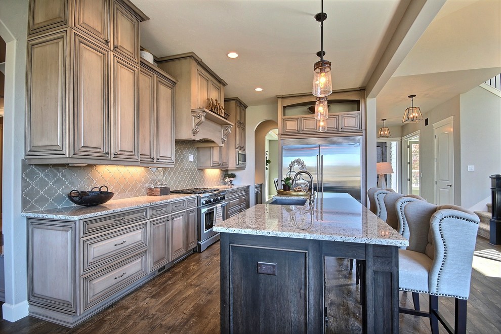 Inspiration for a large craftsman single-wall medium tone wood floor open concept kitchen remodel in Portland with a farmhouse sink, raised-panel cabinets, beige cabinets, granite countertops, green backsplash, glass tile backsplash, stainless steel appliances and an island