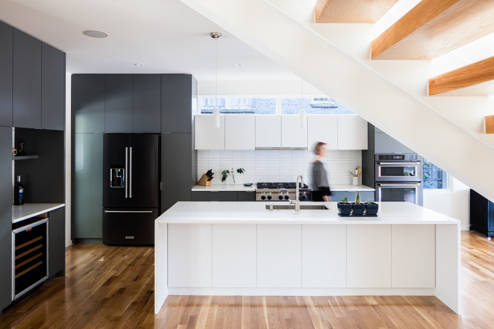 Immagine di una cucina moderna con lavello sottopiano, ante lisce, ante nere, paraspruzzi bianco, elettrodomestici neri, pavimento in legno massello medio, pavimento marrone e top bianco