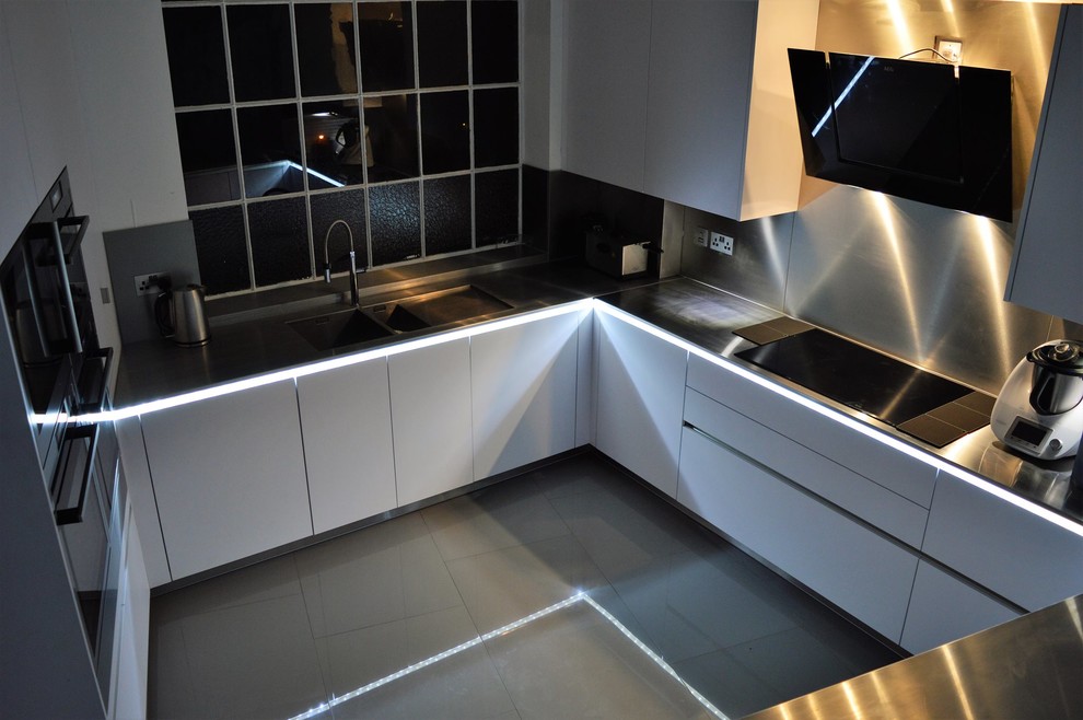 Design ideas for a medium sized industrial u-shaped open plan kitchen in Hertfordshire with an integrated sink, flat-panel cabinets, white cabinets, stainless steel worktops, porcelain flooring and a breakfast bar.