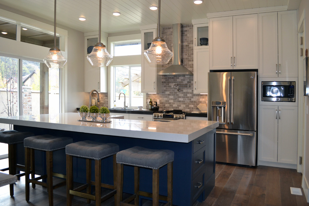 Inspiration for a mid-sized transitional galley medium tone wood floor open concept kitchen remodel in Salt Lake City with an undermount sink, shaker cabinets, white cabinets, quartz countertops, gray backsplash, mosaic tile backsplash, stainless steel appliances and an island