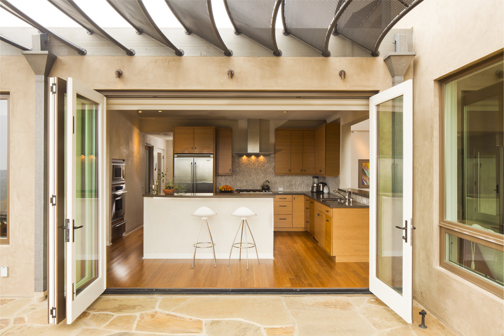 Foto de cocina minimalista de tamaño medio con electrodomésticos de acero inoxidable, puertas de armario de madera oscura, salpicadero de azulejos de piedra, suelo de madera en tonos medios y una isla