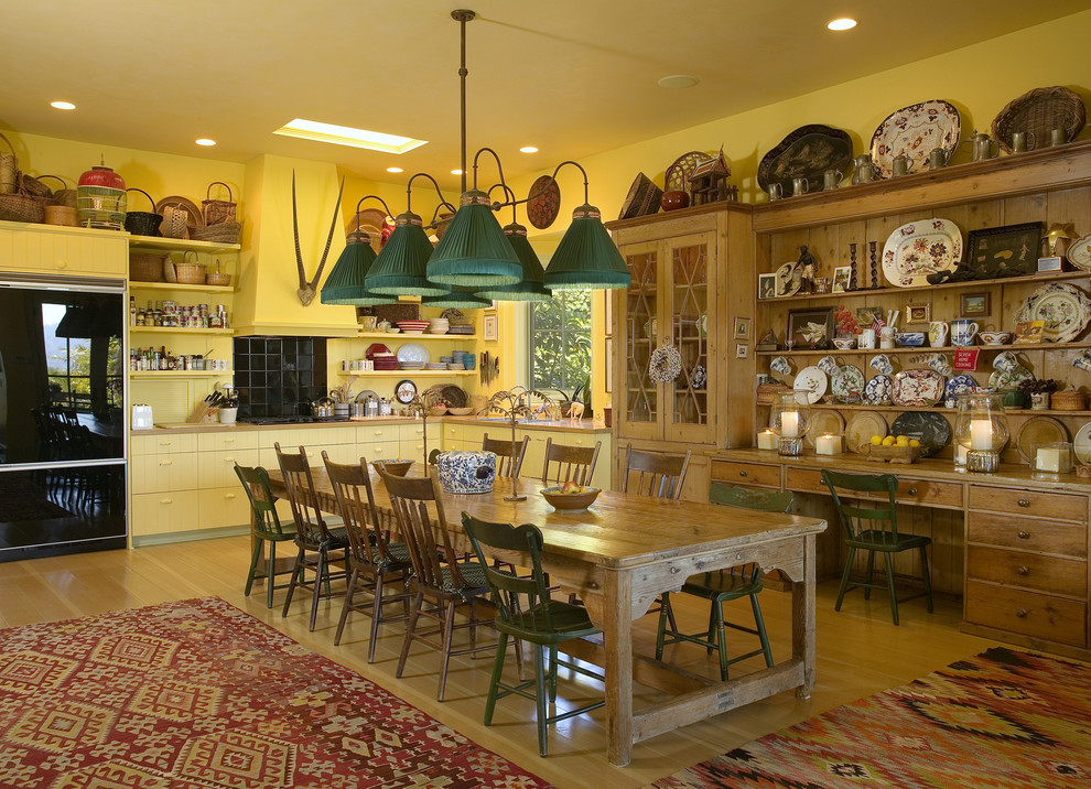 На фото: кухня в стиле фьюжн с обеденным столом, желтыми фасадами и черной техникой