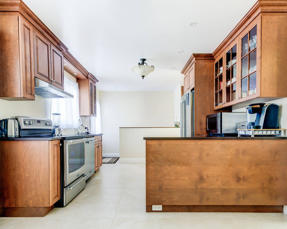 Mittelgroße Klassische Wohnküche in L-Form mit Unterbauwaschbecken, profilierten Schrankfronten, dunklen Holzschränken, Küchengeräten aus Edelstahl, Porzellan-Bodenfliesen, Kücheninsel und Quarzit-Arbeitsplatte in Montreal