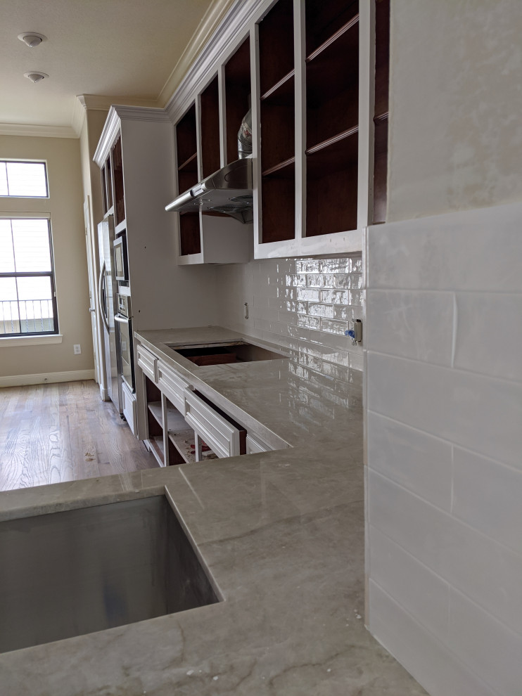 Große Moderne Wohnküche in L-Form mit weißen Schränken, Granit-Arbeitsplatte, Küchenrückwand in Weiß, Rückwand aus Metrofliesen, Küchengeräten aus Edelstahl, gebeiztem Holzboden, Kücheninsel, grauem Boden und weißer Arbeitsplatte in Houston