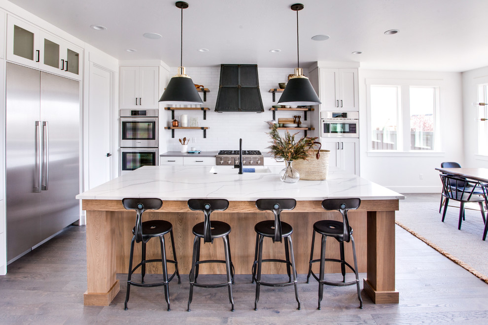 Inspiration for a farmhouse l-shaped light wood floor and beige floor eat-in kitchen remodel in Boise with an undermount sink, shaker cabinets, white cabinets, white backsplash, stainless steel appliances, an island and white countertops