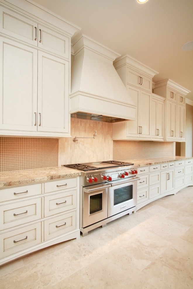Inredning av ett klassiskt stort kök, med luckor med profilerade fronter, vita skåp, granitbänkskiva, rostfria vitvaror, travertin golv och en köksö