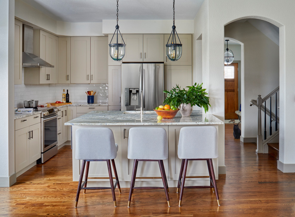 Klassische Küche in L-Form mit Unterbauwaschbecken, Schrankfronten im Shaker-Stil, beigen Schränken, Küchenrückwand in Weiß, Küchengeräten aus Edelstahl, dunklem Holzboden, Kücheninsel, braunem Boden und grauer Arbeitsplatte in Denver
