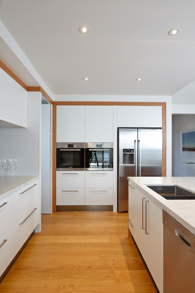 Cette image montre une cuisine ouverte design avec un évier intégré, des portes de placard blanches, plan de travail en marbre, une crédence miroir, un électroménager blanc et un sol en bois brun.