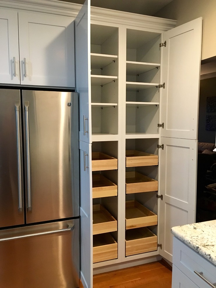 Inspiration for a medium sized classic l-shaped kitchen pantry in DC Metro with a belfast sink, shaker cabinets, white cabinets, granite worktops, grey splashback, stainless steel appliances, medium hardwood flooring, an island and marble splashback.