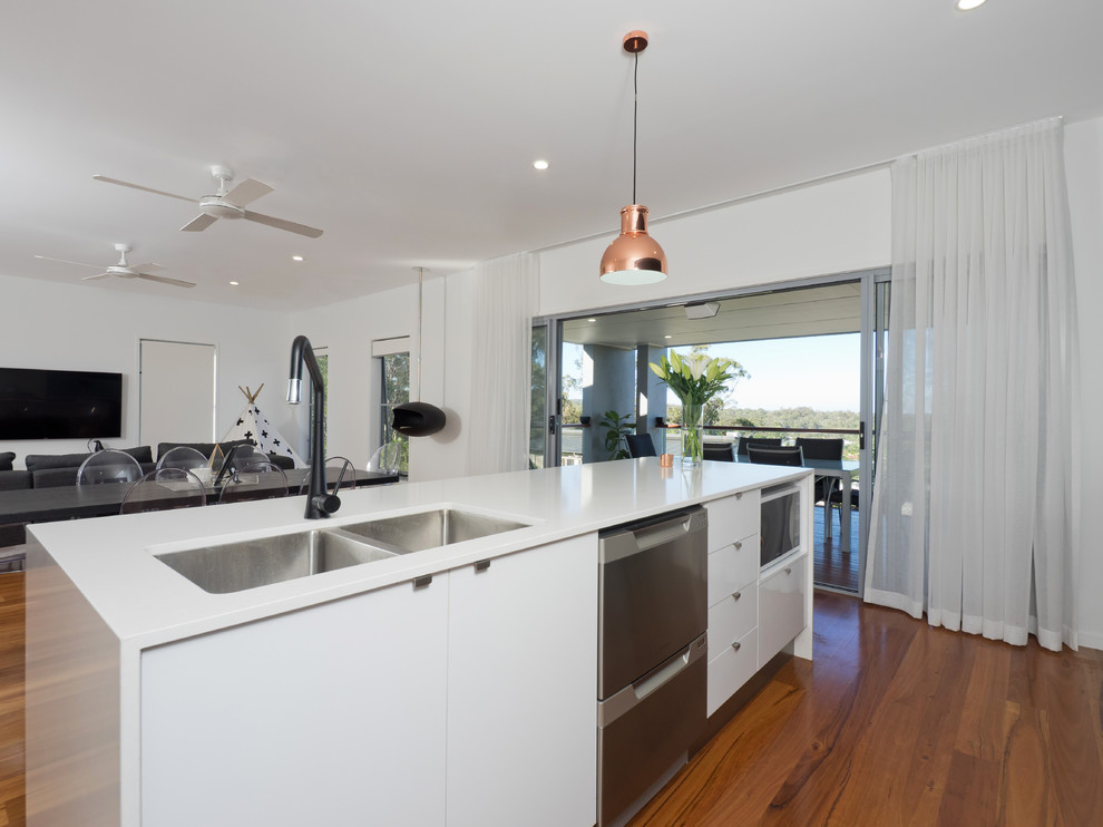 Zweizeilige, Große Moderne Wohnküche mit Einbauwaschbecken, weißen Schränken, Granit-Arbeitsplatte, Küchenrückwand in Weiß, Glasrückwand, Küchengeräten aus Edelstahl, hellem Holzboden und Kücheninsel in Brisbane