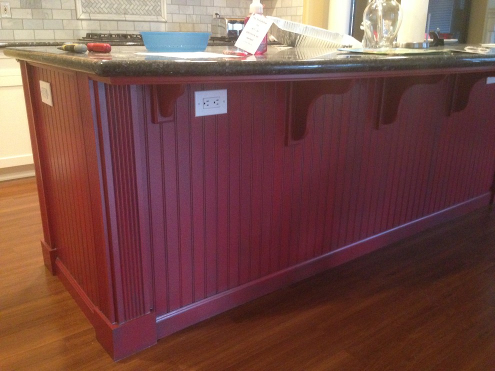 Exemple d'une cuisine linéaire chic en bois clair de taille moyenne avec un placard avec porte à panneau encastré, un plan de travail en granite, une crédence grise, un électroménager noir et un sol en bois brun.