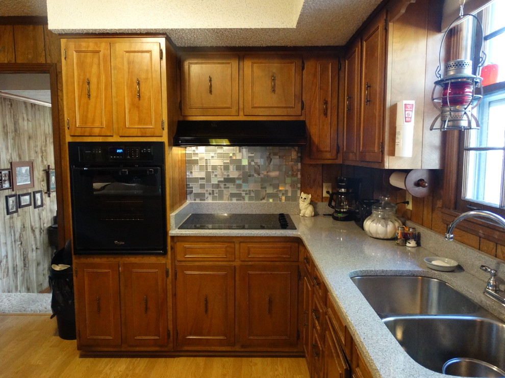 Idéer för mellanstora vintage grått kök, med en dubbel diskho, granitbänkskiva, flerfärgad stänkskydd, stänkskydd i glaskakel, svarta vitvaror, en köksö, luckor med infälld panel, skåp i mellenmörkt trä, mellanmörkt trägolv och brunt golv