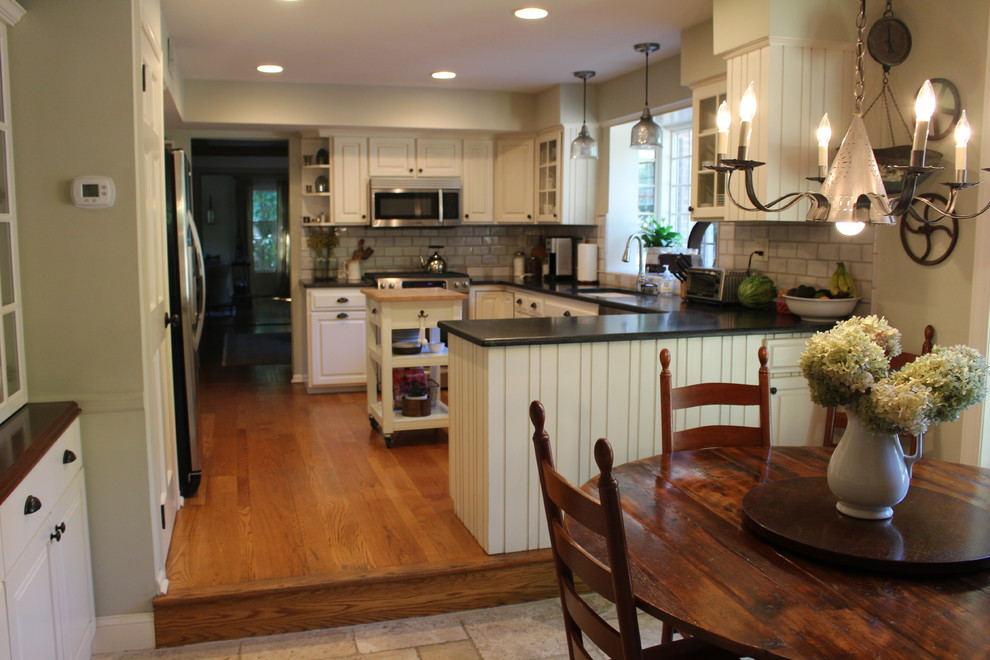 Example of a mid-sized country u-shaped medium tone wood floor and beige floor eat-in kitchen design in Philadelphia with an undermount sink, raised-panel cabinets, white cabinets, granite countertops, white backsplash, terra-cotta backsplash, stainless steel appliances and an island