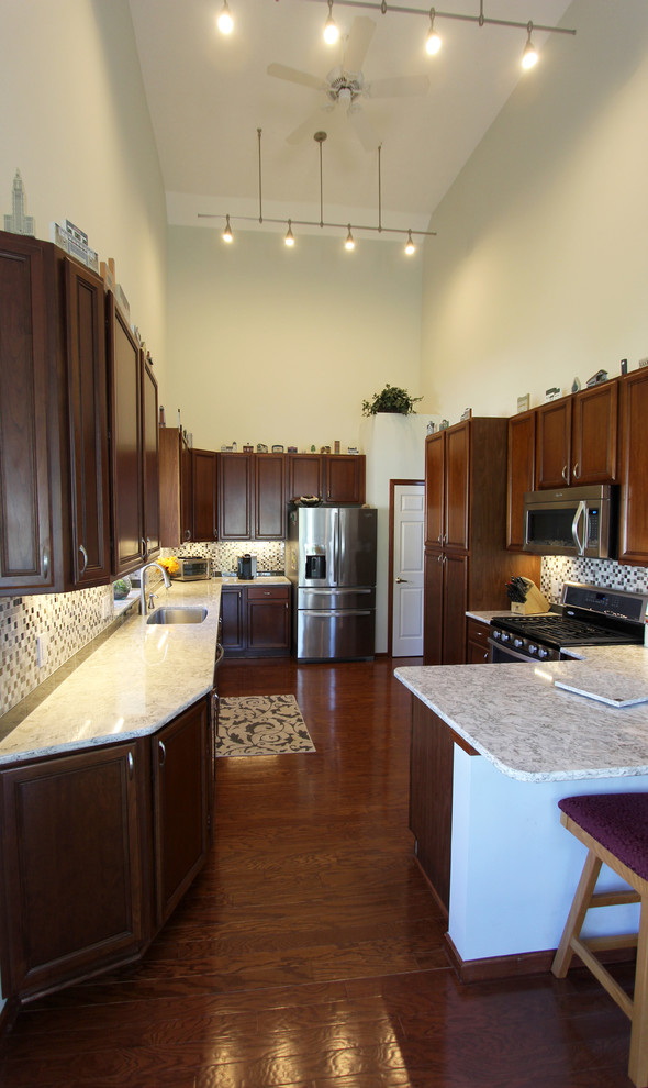 Photo of a large classic l-shaped kitchen/diner in Cleveland with a single-bowl sink, raised-panel cabinets, dark wood cabinets, grey splashback, glass tiled splashback, black appliances, dark hardwood flooring and no island.