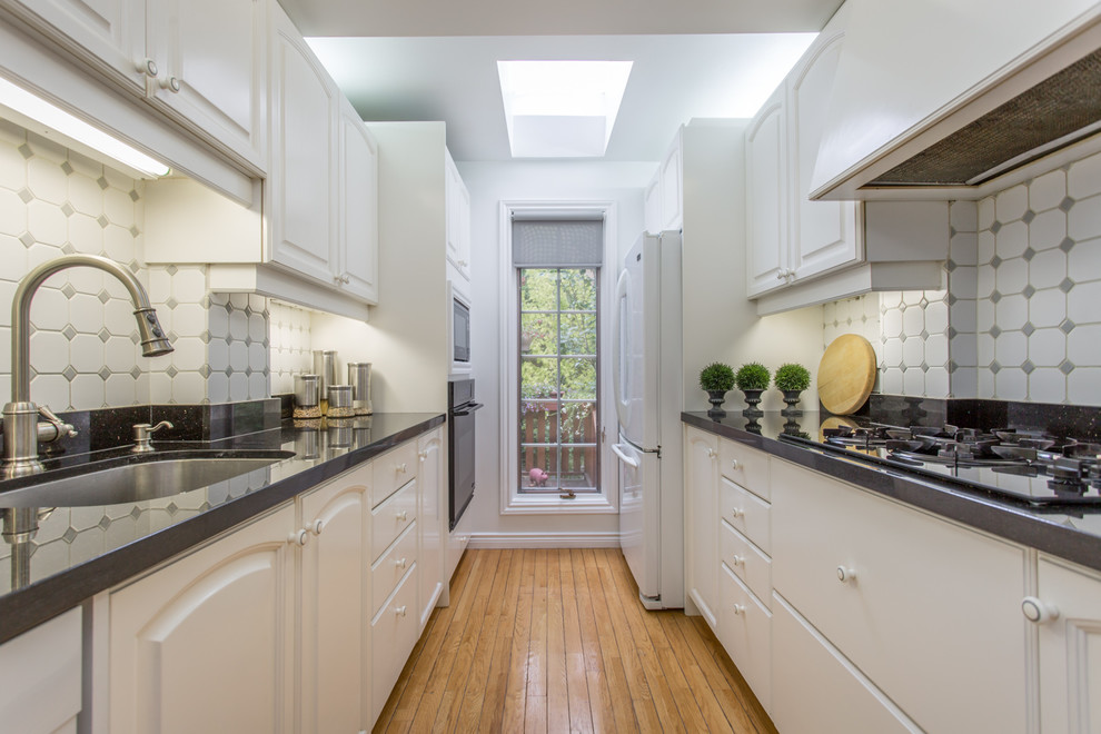 Design ideas for a large traditional galley enclosed kitchen in Toronto with ceramic splashback, white appliances, a submerged sink, beaded cabinets, white splashback, medium hardwood flooring, no island, white cabinets and granite worktops.