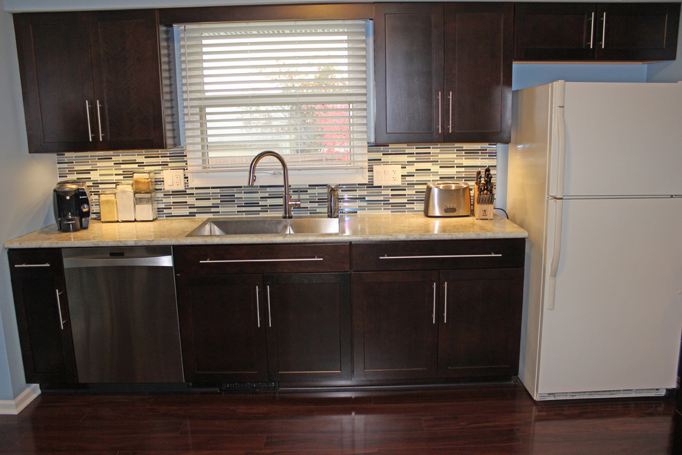 Photo of a classic kitchen/diner in Cleveland with a submerged sink, raised-panel cabinets, brown cabinets, laminate countertops, blue splashback, glass tiled splashback and white appliances.
