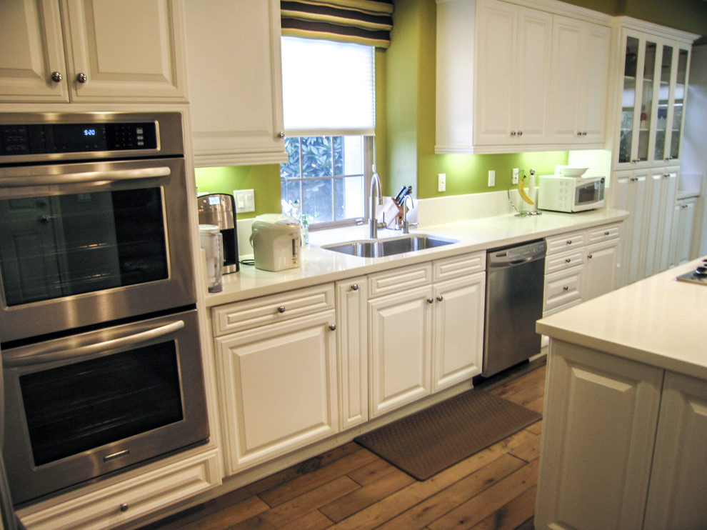 Modern inredning av ett mellanstort kök, med en undermonterad diskho, luckor med upphöjd panel, vita skåp, bänkskiva i kvartsit, grönt stänkskydd, stänkskydd i sten, rostfria vitvaror, ljust trägolv och en köksö