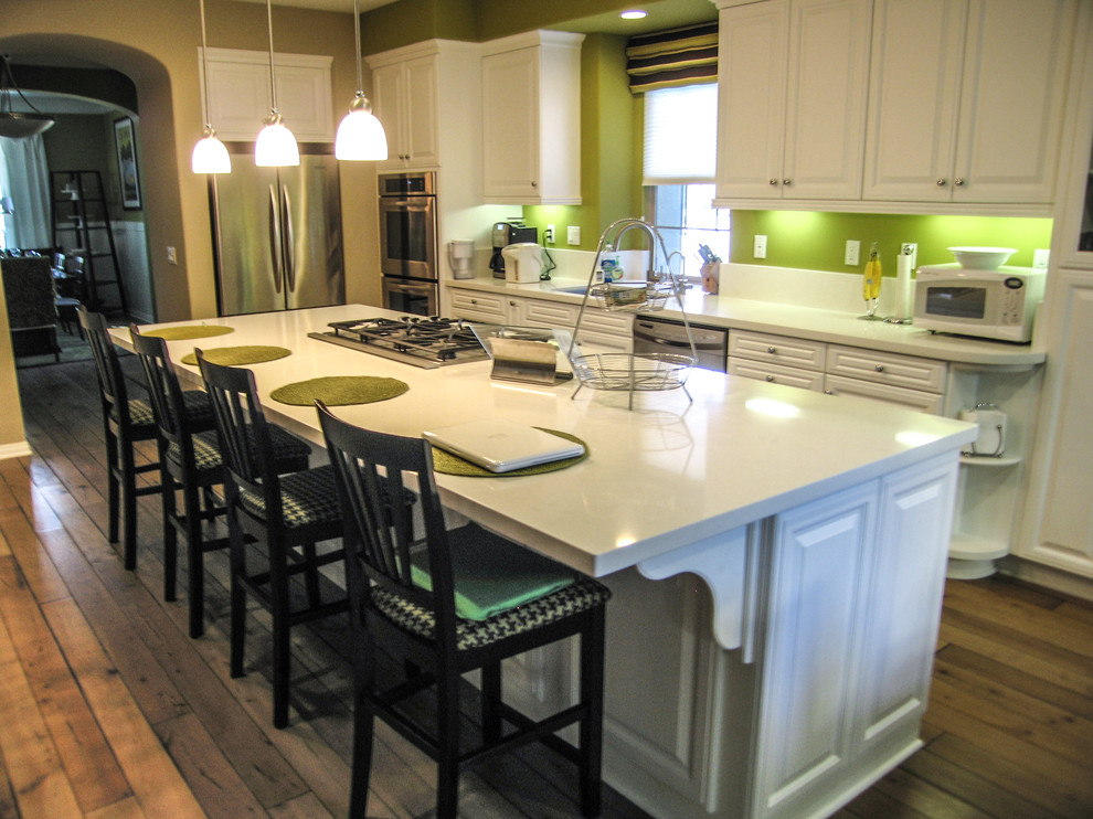 Inredning av ett modernt mellanstort kök, med en undermonterad diskho, luckor med upphöjd panel, vita skåp, bänkskiva i kvartsit, grönt stänkskydd, stänkskydd i sten, rostfria vitvaror, ljust trägolv och en köksö