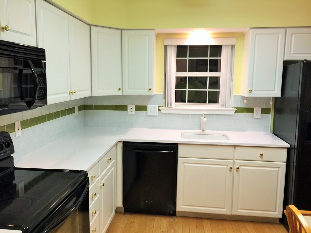 Medium sized classic l-shaped kitchen/diner in Philadelphia with a built-in sink, raised-panel cabinets, white cabinets, engineered stone countertops, white splashback, glass tiled splashback, black appliances and bamboo flooring.
