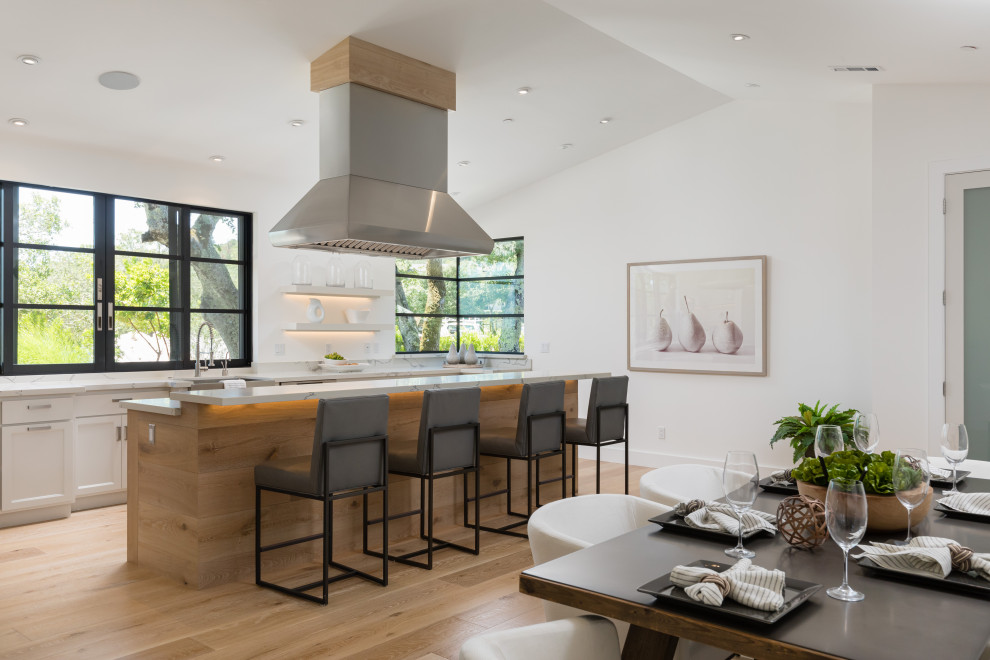 Example of a transitional galley light wood floor, beige floor and vaulted ceiling eat-in kitchen design in San Francisco with a farmhouse sink, shaker cabinets, white cabinets, an island and white countertops