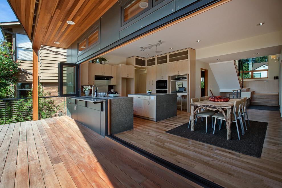 Exemple d'une cuisine américaine tendance en U et bois clair de taille moyenne avec un placard à porte plane, un plan de travail en verre recyclé, un électroménager noir, parquet clair, îlot, une crédence rouge, une crédence en carreau de verre et un évier encastré.