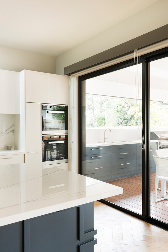 Design ideas for a large contemporary open plan kitchen in Melbourne with a double-bowl sink, white cabinets, tile countertops, white splashback, porcelain splashback, stainless steel appliances, medium hardwood flooring, an island, beige floors and white worktops.
