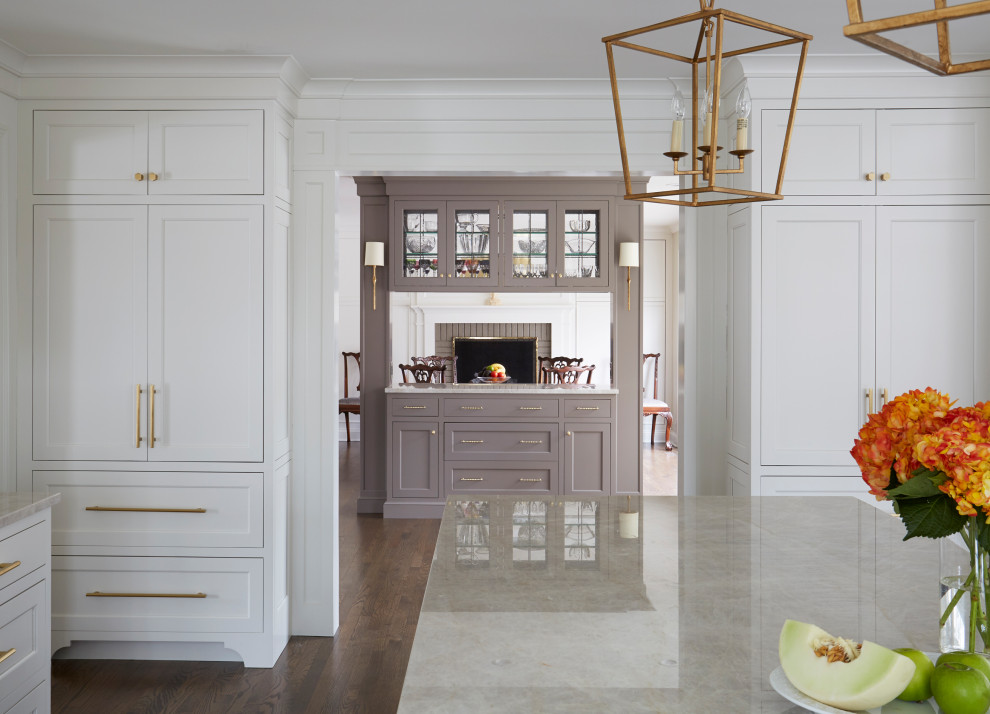 Inredning av ett klassiskt stort beige beige kök, med en undermonterad diskho, luckor med infälld panel, vita skåp, marmorbänkskiva, vitt stänkskydd, stänkskydd i keramik, rostfria vitvaror, mellanmörkt trägolv, en köksö och brunt golv
